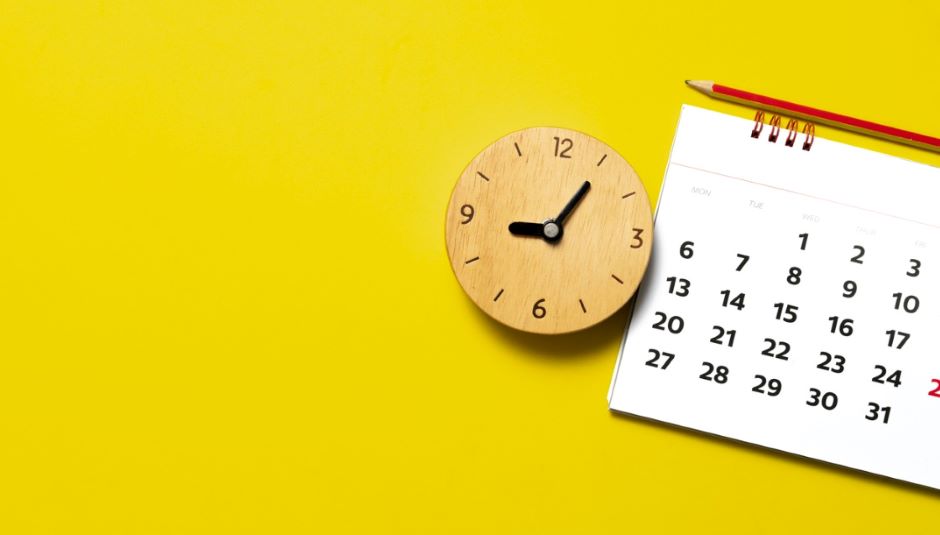 A close-up of a wooden clock and calendar on a yellow table.